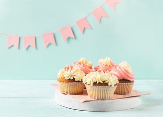 Muffins are decorated with thick white and pink cream on a light blue background pink festive flags. Festive concept.
