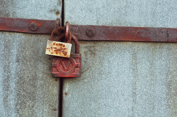 Fototapeta na wymiar background of old gray metal gates closed on two rusty padlocks