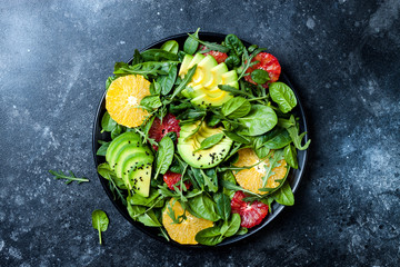 Citrus salad with mixed greens and blood orange on black ceramic plate. Vegan, vegetarian, clean eating, dieting, food concept. Dark stone background.