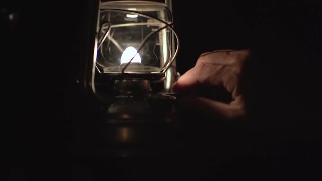 Male hand turns flame down on storm lamp