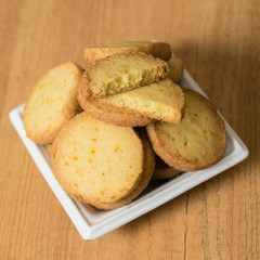 Homemade lemon cookies in a white saucer on a wooden table. Square picture, closeup.
