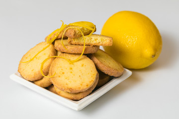Homemade lemon cookies in a white saucer near fresh lemon on white background. Closeup, isolated
