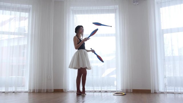 Young woman ballerina performs circus juggling standing near the window