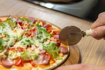 Closeup hand of chef baker in white uniform cutting pizza at kitchen, soft selective focus.