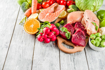 Trendy pegan diet - vegan plus paleo diet food concept, many fresh vegetables, fruits, raw beef and chicken meat, salmon fish, white wooden background top view copy space