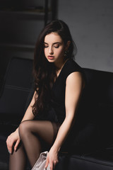 Fototapeta na wymiar attractive brunette woman in elegant dress sitting on couch on dark background