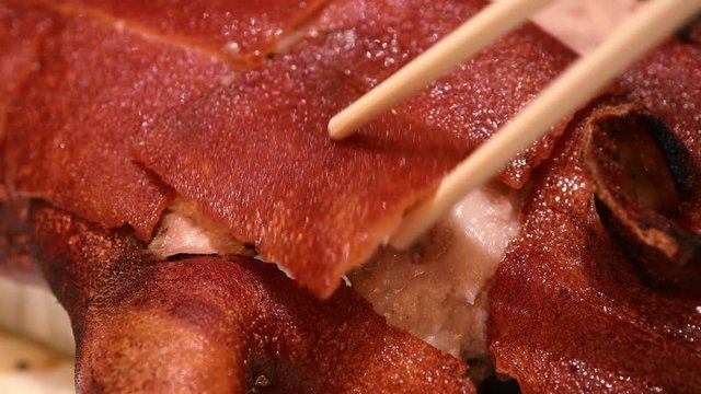 Footage of a hand using chopsticks  to eat barbecued suckling pig  