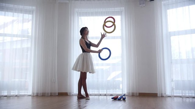 Young woman ballerina juggling with a circle objects in bright studio by the window
