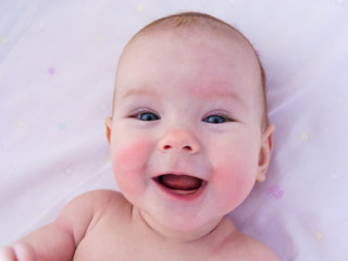 Little cheerful baby girl baby takes sun and air baths, skin dipping. The baby has redness on the cheeks, similar to frostbite.