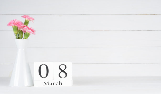 Womens day concept, happy womens day, international women's day. Pink carnation flower in vase with March 8 text on wooden calendar on white wooden background.