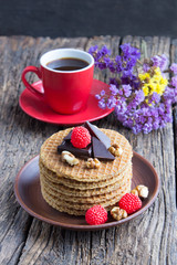 Delicious dutch waffles with chocolate, nuts, berries, flowers and cup of coffee on a dark wooden background. Vertical view. Close-up