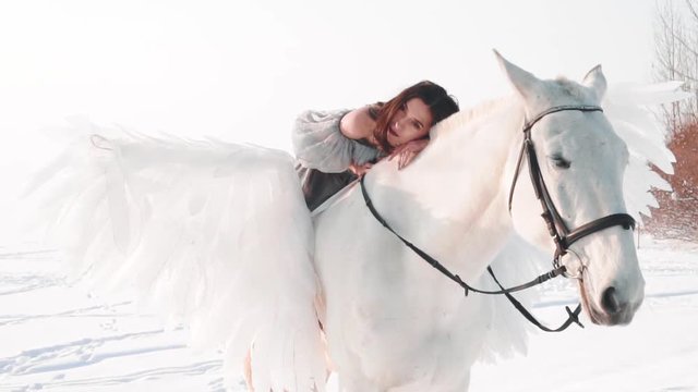 charming pretty dark-haired lady in a long gray vintage dress with bare shoulders sits astride horse, tenderly lies on the animal and looks playfully at camera, pretty woman is on zine landscape