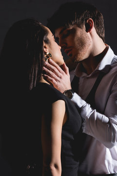 man in white shirt and woman in black dress kissing on black background