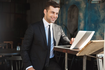 Happy young businessman sitting in cafe using laptop computer.