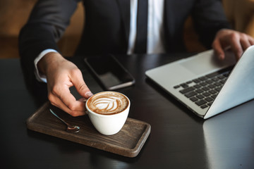 Handsome young businessman sitting in cafe using laptop computer drinking coffee.