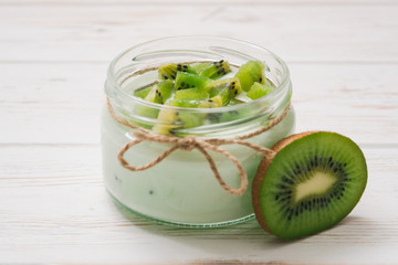 Yogurt with kiwi slices on a wooden white background.