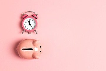 Piggy bank and classic alarm clock on pink background. Time to saving, money, banking concept.