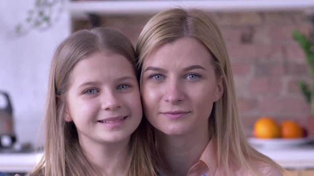 portrait of caring sisters, lovely small and adult girls with blue eyes are smiling and looking at camera close-up at home