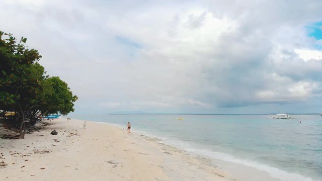 Aerial view of woman walking through the beach in Balicasag Island, Panglao, Bohol, Philippines. Coral reef, white beach, palm trees, turquoise water, paradise island / 4K Drone Video