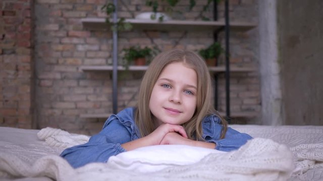 portrait of lovely child girl with blue eyes lying on pillow on bed in room at home