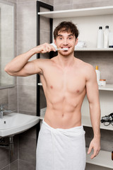 handsome man in towel brushing teeth and looking at camera
