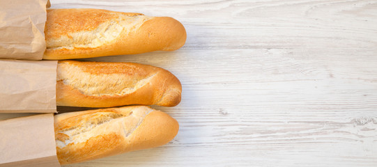 French baguettes in paper bags on white wooden background, top view. Space for text.