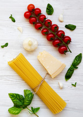 Spaghetti, tomatoes, basil, parmesan, garlic. Ingredients for cooking pasta on a white wooden background, flat lay. From above.
