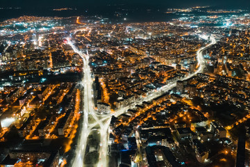 Aerial view of the resort town of Varna, Bulgaria at sunset of the day late in the evening. Bright lights of street lamps. Highways with car lights. Evening sky. The texture of the glowing night city