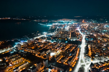 Aerial view of the resort town of Varna, Bulgaria at sunset of the day late in the evening. Bright lights of street lamps. Highways with car lights. Evening sky. The texture of the glowing night city