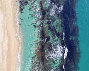 Scenic aerial view of golden sand and transparent turquoise sea water with white foam and splashes from small waves with underwater stones. The concept of a summer holiday. Drone