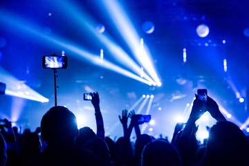 Silhouettes of crowds of spectators at a concert with smartphones in their hands.