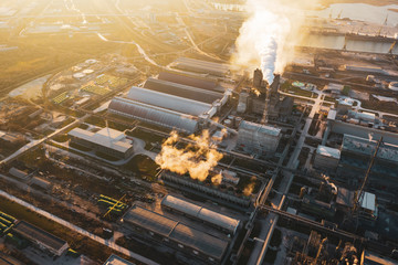 Aerial view, the vast territory of a large industrial chemical plant with high pipes in the bright light of winter sunset. Thick smoke comes from a high pipe. Environmental pollution. Drone