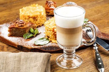A freshly prepared Cup of frothy lette coffee is served with a piece of cake. On a wooden table.
