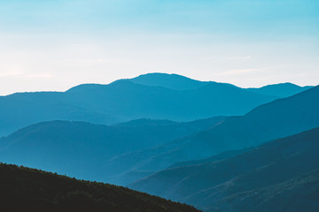 Landscape of mountains against the blue sky and clouds. Forest of pine trees. The tops of the mountains in the winter in a small haze. Panorama of the peaks of the beautiful tree-covered mountains