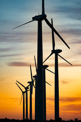 The movement of wind turbines blades in the field against the backdrop of a bright orange sunset...