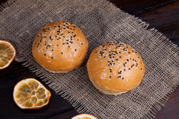 Hot sweet buns on a rustic wood background. Shaped food with sesame on fabric and dry oranges