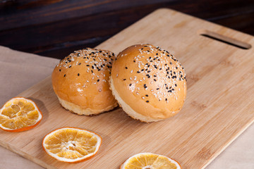 Hot sweet buns on a rustic background. Shaped food with sesame on cutting board around with dry oranges