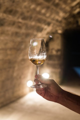 Glass of white wine in mans hand in wine cellar