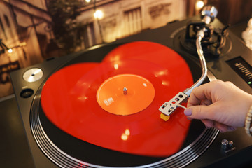 Red vinyl in the shape of a heart on a festive background with bokeh lights. The hand of the girl...