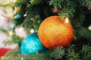 Christmas card. Christmas picture. Bright sparkling orange ball on fluffy branches of a Christmas tree. Background bokeh lights of garland. Ready Christmas background for your text. Glitter.