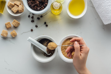 partial view of woman adding brown sugar into pounder with ground coffee on white surface