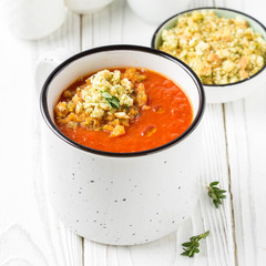 Tomato cream soup in white mug, red hot soup in cup with fragrant breadcrumbs,  olive oil. Vegetarian vegetable lunch on wooden background
