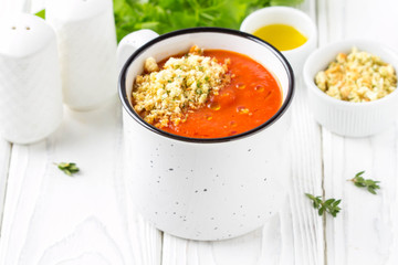 Tomato cream soup in white mug, red hot soup in cup with fragrant breadcrumbs,  olive oil. Vegetarian vegetable lunch on wooden background