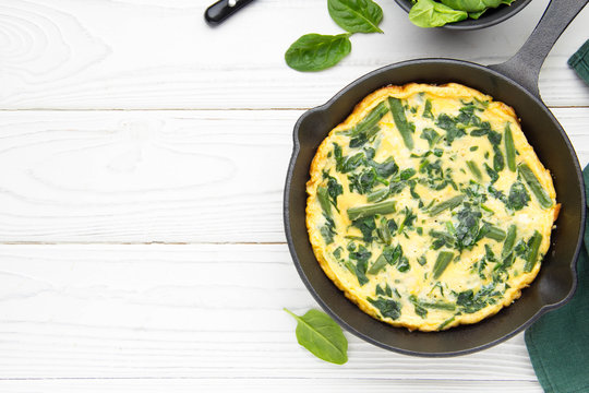 Omelet with spinach and green beans, healthy food. Egg and milk Frittata, delicious Breakfast. In black frying pan on white wooden background with copyspace