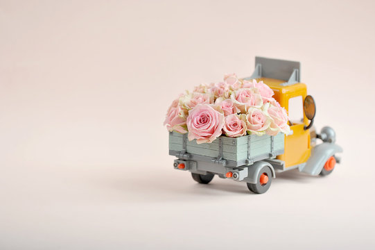 Roses in the back of a toy truck. Free space to place text. The concept of holiday greetings. Light background.