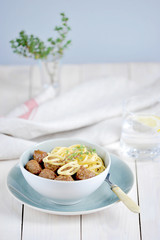 Meatballs with bavette pasta in a deep bowl. A sprig of thyme decorates the dish. Light wooden background. Vertical frame orientation.