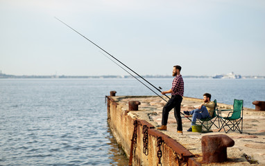 leisure and people concept - happy friends with fishing rods on pier at sea