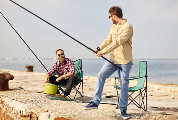 leisure and people concept - happy friends with fishing rods on pier at sea