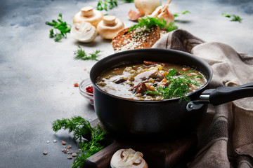 Hot thick mushroom soup with beef, spices and wholegrain barley, meat broth. With black bread, in metal pan, top view, flat lay, gray kitchen table backgound