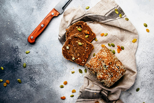 Whole wheat organic rye dark bread with pumpkin seeds, dried fruit, raisins and sesame seeds on gray towel on the kitchen table background, top view. Space for text